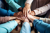 A group of hands from all osrts of ages and backgrounds doing a team hand gesture in the center